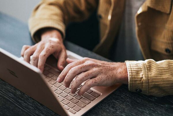 Close-up of hands typing on a sleek laptop, showcasing a modern workspace with a wooden table.
